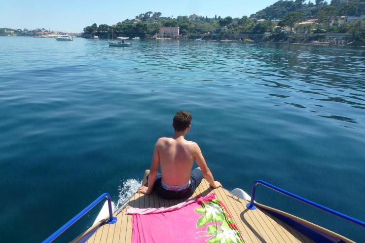 Person sitting on a boat deck facing the sea with a pink towel beside them.