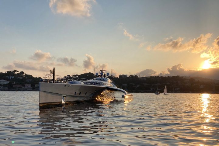 Catamaran on calm water at sunset with hills and clouds in the background.
