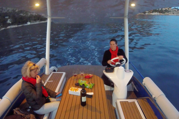 Two people on a boat with snacks and drinks, one steering, with scenic water view.
