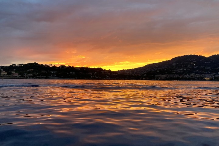 Scenic sunset over a calm sea with hills silhouetted in the background.