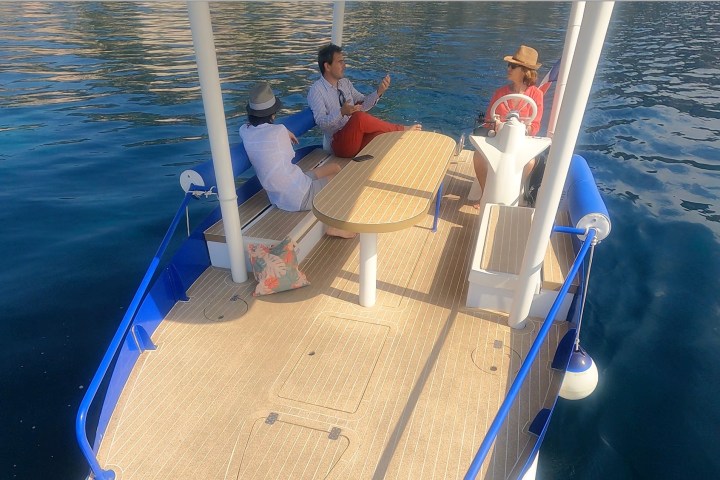 Three people sitting on a boat with a table, talking and enjoying sunny weather.