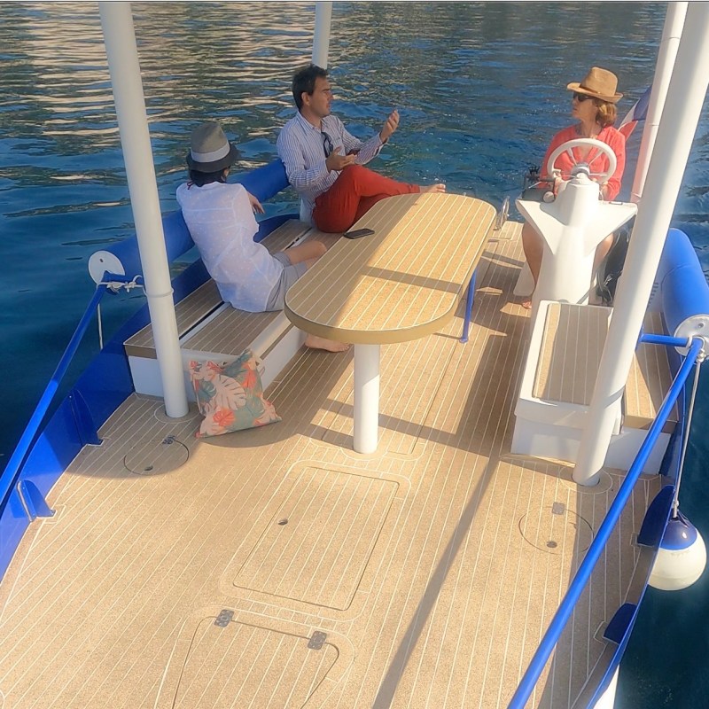 Three people sitting on a boat with a table, talking and enjoying sunny weather.
