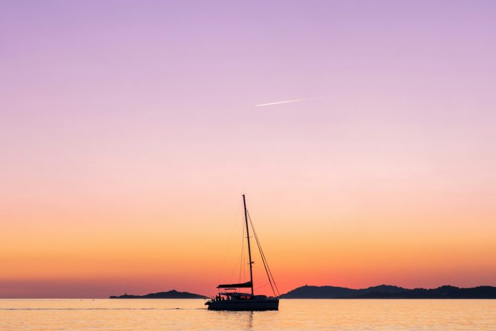 Sailboat on calm sea at sunset with colorful sky and distant hills.