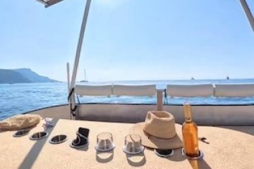Boat deck with table, hat, and bottle; ocean view with solar panels overhead.