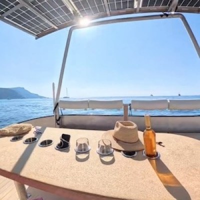 Boat deck with table, hat, and bottle; ocean view with solar panels overhead.