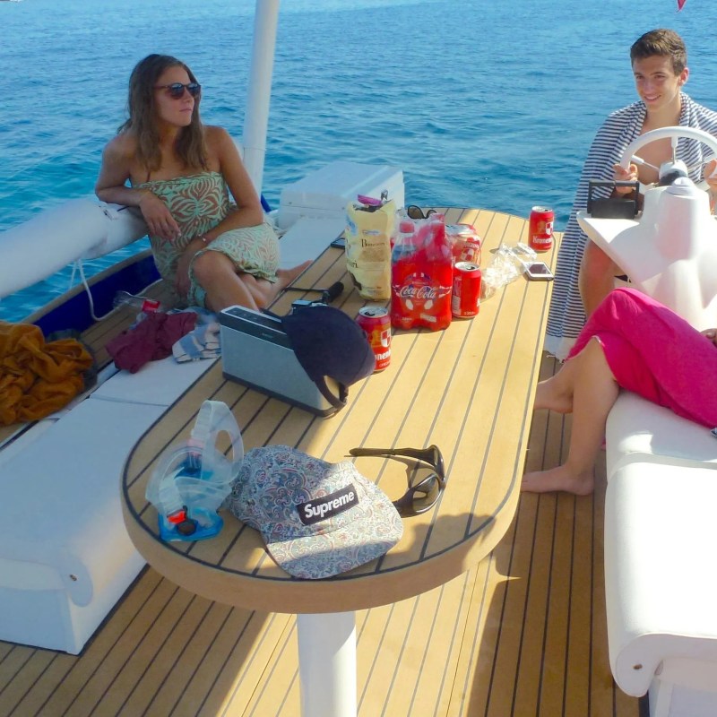 Group of people relaxing on a boat with snacks and drinks, surrounded by ocean.