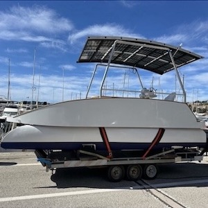 Medium-sized catamaran with canopy on a trailer at a marina.