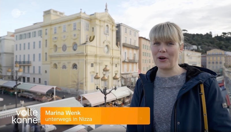Woman stands outside with a European cityscape background and an information bar at the bottom.