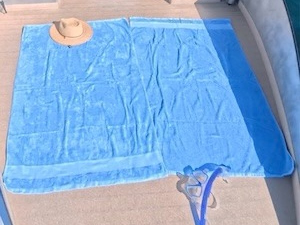 Two blue towels and a straw hat on a boat deck with a view of the water.