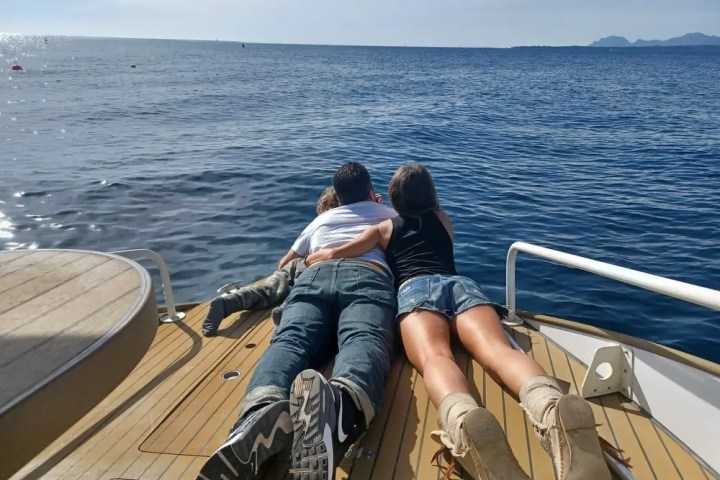 Three people lying on a boat deck, facing the sea with distant mountains.