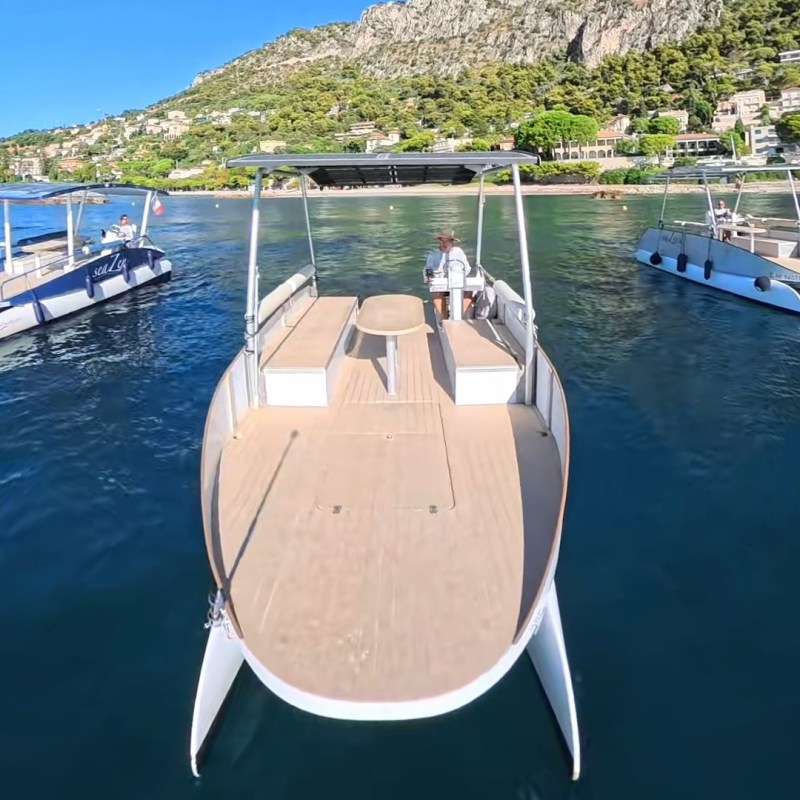Three solar-powered boats on clear water near a rocky coastline.