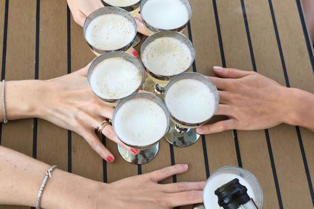 Four hands clinking six glasses of champagne over a wooden table.