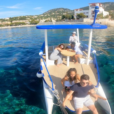 Group of people relaxing on a boat in clear blue water near a coastal town.