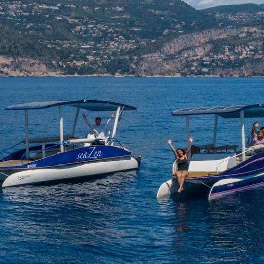 Two small boats with passengers on a calm sea near a rocky coastline.