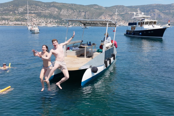 Two people jumping off a boat into the water with mountains in background.