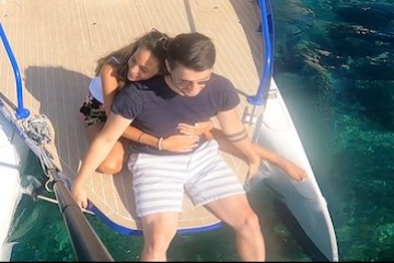 Couple sitting on a boat's edge, hugging near clear blue water.
