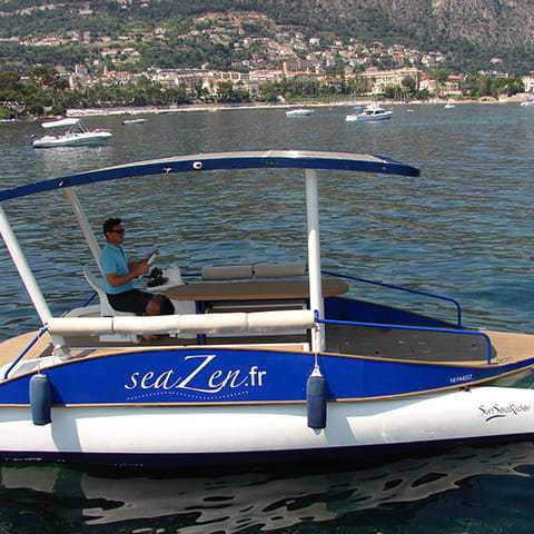 Man on a solar-powered boat with canopy floats on a scenic lake.
