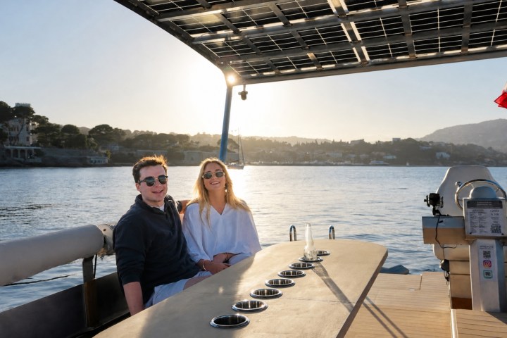 Two people sitting on a SeaZen boat with a scenic view of the Côte d'Azur at sunset.