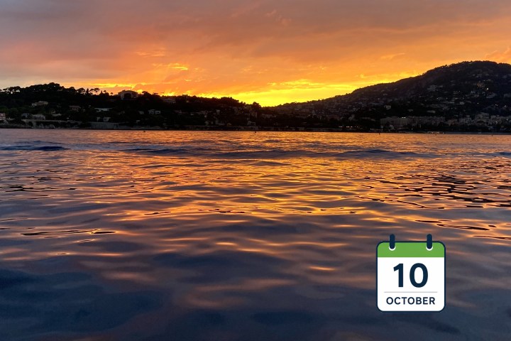 Sunset over a calm sea with hills silhouetted.